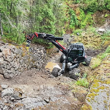 Menzi Muck maskin løfter stein i skogbakke
